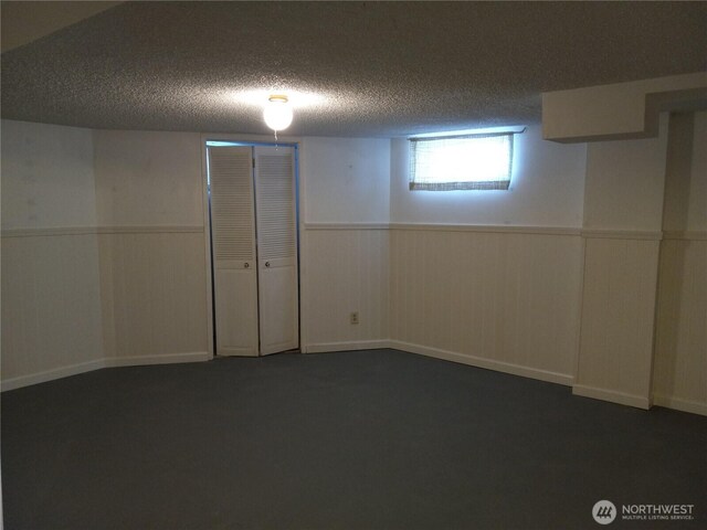 basement with dark colored carpet, a textured ceiling, and wainscoting