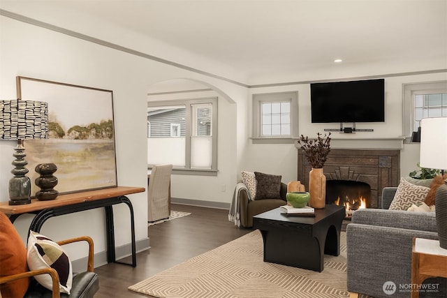 living room featuring dark wood-type flooring, plenty of natural light, arched walkways, and a lit fireplace