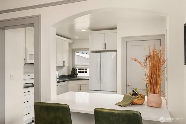 kitchen featuring a sink, white appliances, arched walkways, and white cabinets