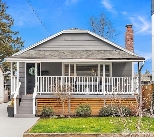 view of front of home featuring covered porch, a chimney, and roof with shingles