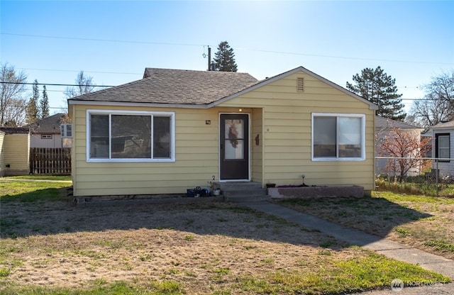 bungalow-style home featuring entry steps, a shingled roof, fence, and a front lawn