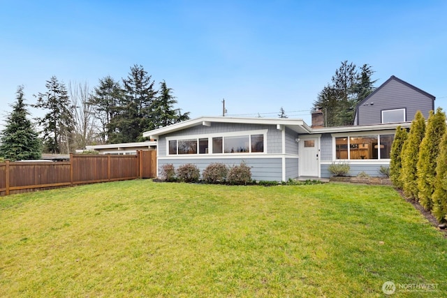 rear view of house featuring a yard, a chimney, and fence