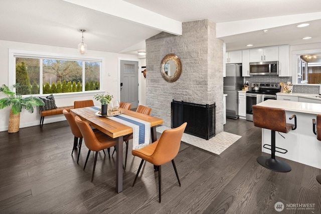 dining room with vaulted ceiling with beams, recessed lighting, dark wood-type flooring, a large fireplace, and baseboards