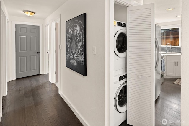 clothes washing area featuring a sink, stacked washer and dryer, dark wood finished floors, and laundry area