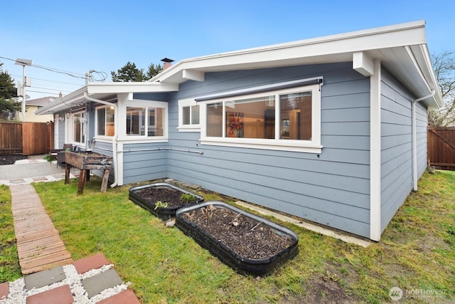 view of side of property featuring a vegetable garden, a lawn, and fence