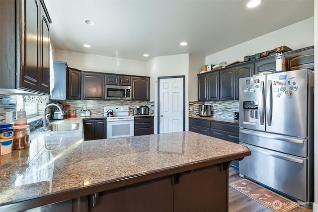 kitchen featuring dark brown cabinetry, decorative backsplash, appliances with stainless steel finishes, a peninsula, and a sink