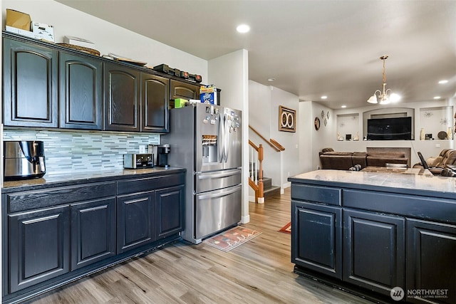 kitchen featuring tasteful backsplash, stainless steel fridge with ice dispenser, open floor plan, hanging light fixtures, and light wood-style floors