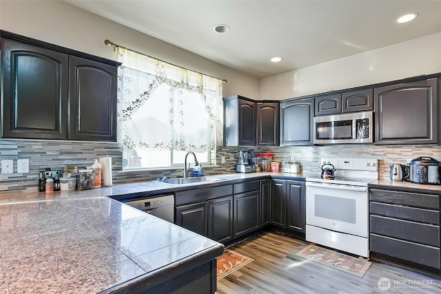 kitchen featuring stainless steel appliances, recessed lighting, tasteful backsplash, a sink, and light wood-type flooring