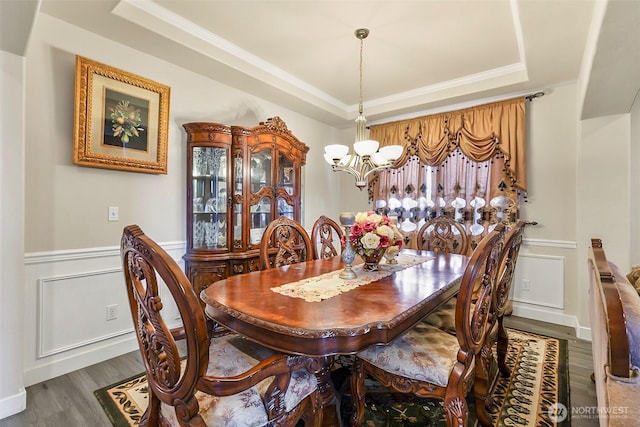 dining area featuring a raised ceiling, wainscoting, an inviting chandelier, and wood finished floors