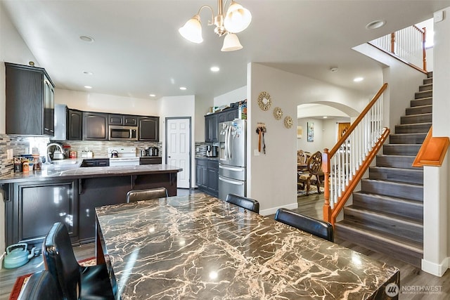 kitchen featuring arched walkways, tasteful backsplash, dark countertops, appliances with stainless steel finishes, and a peninsula