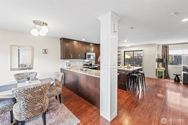 kitchen with tasteful backsplash, dark brown cabinetry, a breakfast bar, wood finished floors, and stainless steel appliances