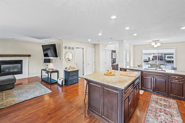 kitchen featuring dark wood finished floors, a sink, a glass covered fireplace, open floor plan, and a center island