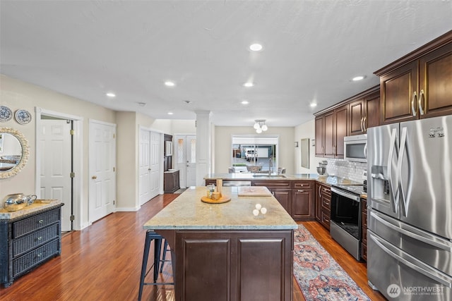 kitchen featuring a kitchen bar, a sink, a center island, stainless steel appliances, and decorative columns