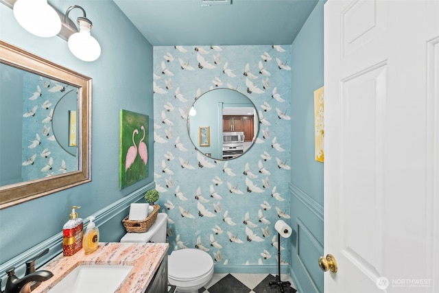 half bath featuring wallpapered walls, toilet, and a sink