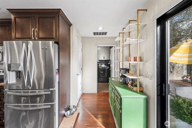 kitchen with visible vents, dark brown cabinets, washer / dryer, wood finished floors, and stainless steel fridge