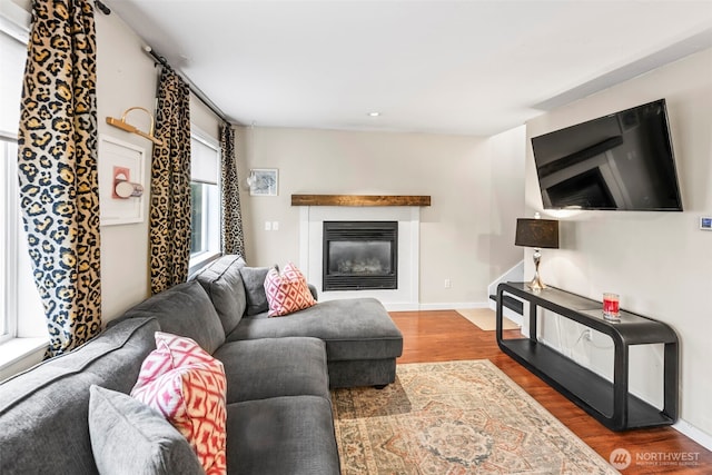 living room with a glass covered fireplace, baseboards, and wood finished floors