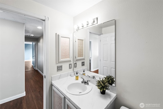 half bath with baseboards, wood finished floors, and vanity