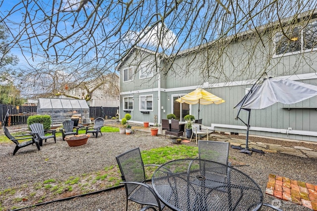 rear view of property with outdoor dining space, fence, a greenhouse, a fire pit, and an outdoor structure