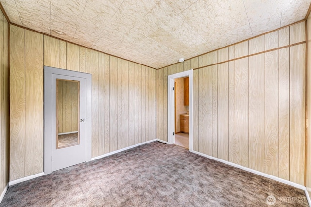 spare room with wood walls, baseboards, and dark carpet