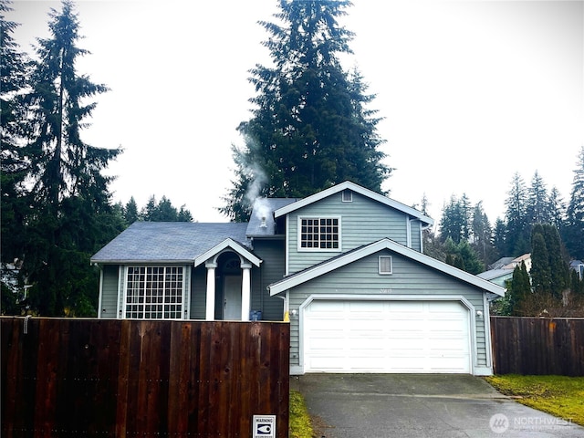 tri-level home featuring driveway, a fenced front yard, and a garage