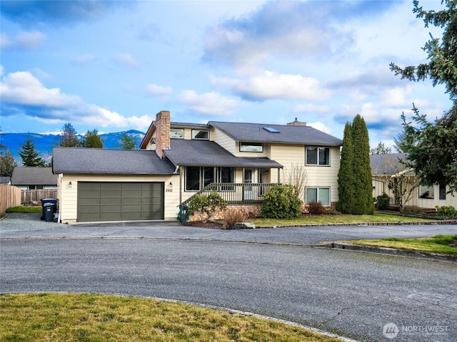 split level home with aphalt driveway, a garage, covered porch, fence, and a chimney