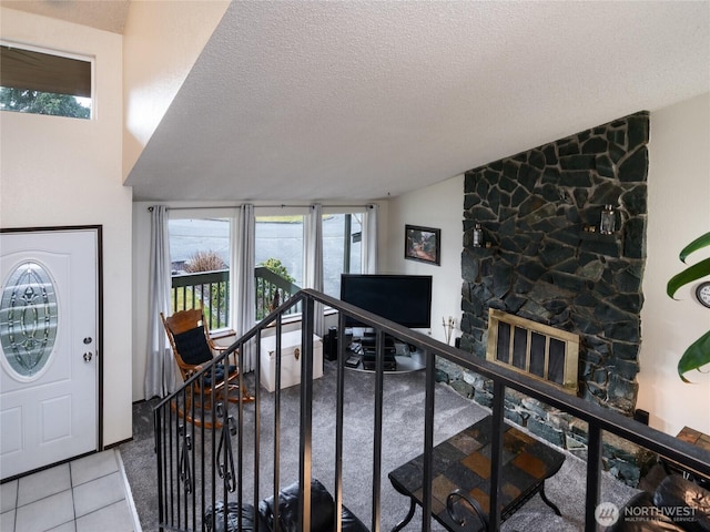 entrance foyer featuring light tile patterned floors, lofted ceiling, stairway, a textured ceiling, and a stone fireplace