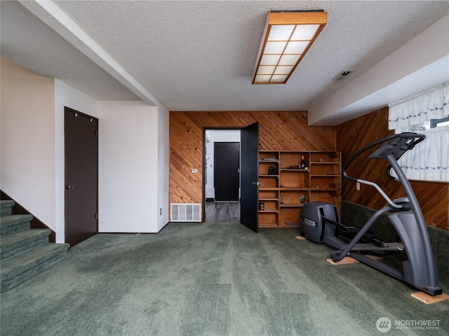 exercise area featuring dark colored carpet, visible vents, wood walls, and a textured ceiling