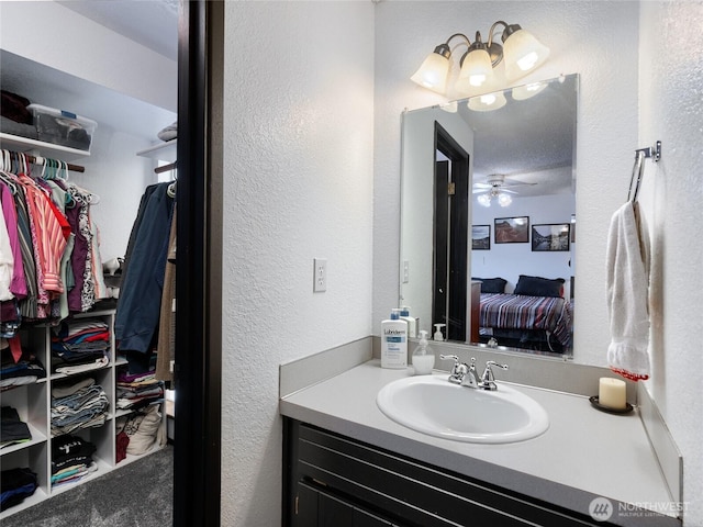 bathroom with a textured wall, vanity, a ceiling fan, a walk in closet, and ensuite bath