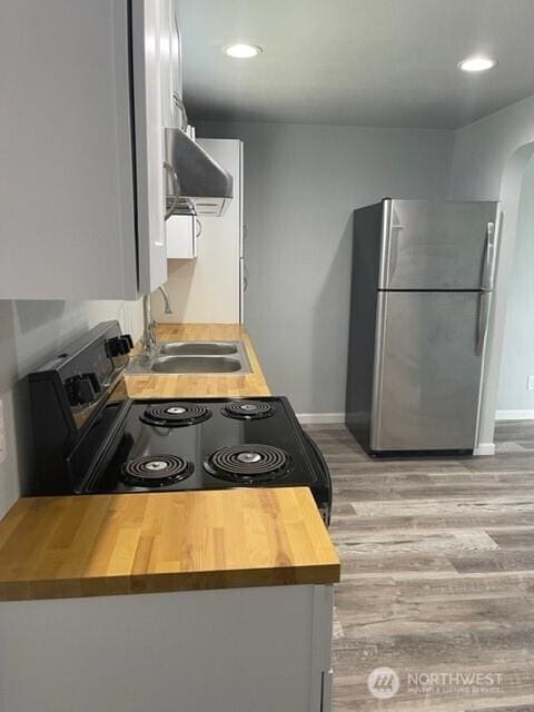 kitchen featuring arched walkways, black range with electric stovetop, freestanding refrigerator, range hood, and a sink