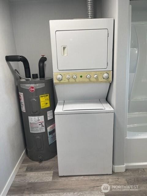 clothes washing area featuring laundry area, electric water heater, stacked washing maching and dryer, and wood finished floors