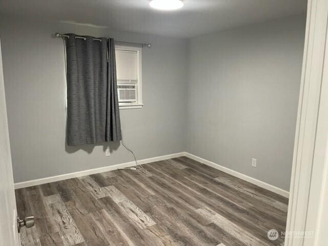 unfurnished room featuring dark wood-style flooring, cooling unit, and baseboards