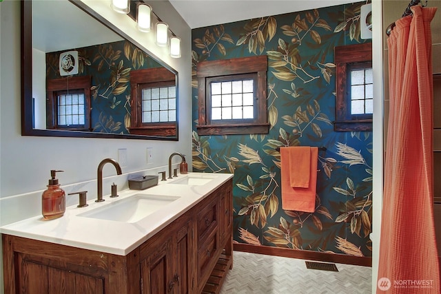 bathroom featuring a healthy amount of sunlight, a sink, and wallpapered walls