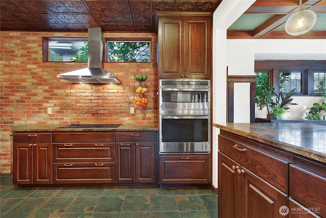 kitchen with island exhaust hood, black electric stovetop, dark stone counters, and stainless steel double oven