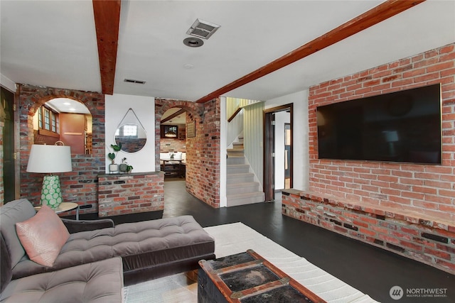 living area featuring visible vents, beamed ceiling, stairway, and brick wall