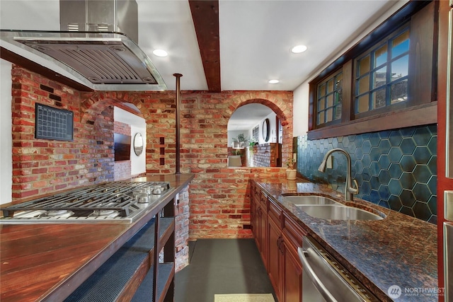 kitchen featuring island exhaust hood, stainless steel appliances, glass insert cabinets, a sink, and dark stone countertops