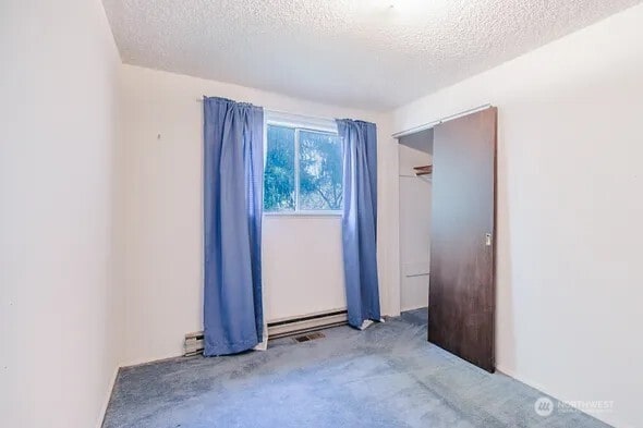 unfurnished bedroom featuring a textured ceiling, a baseboard radiator, and carpet flooring