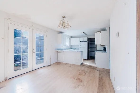 kitchen with freestanding refrigerator, a peninsula, french doors, white cabinetry, and a notable chandelier