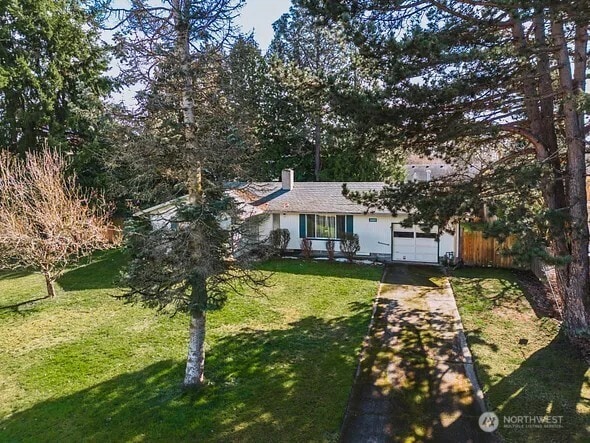 view of front facade with an attached garage, driveway, a chimney, and a front yard