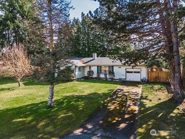 ranch-style house with a garage, fence, concrete driveway, a front lawn, and a chimney