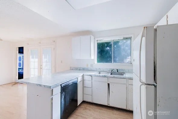 kitchen with white cabinets, dishwasher, freestanding refrigerator, a peninsula, and a sink