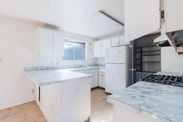 kitchen with light countertops, freestanding refrigerator, white cabinets, a sink, and a peninsula