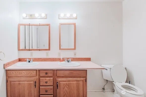 bathroom with toilet, double vanity, and a sink