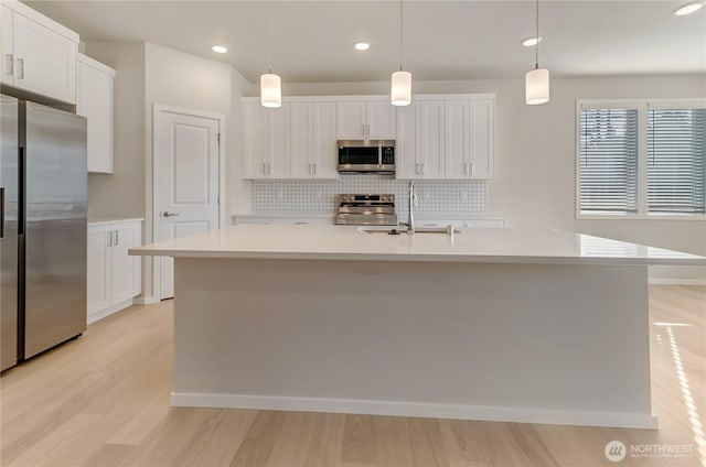 3467 183rd Street Ct E, Tacoma, WA 98446 - kitchen with white cabinets, hanging light fixtures, a kitchen island with sink, stainless steel appliances, and light countertops