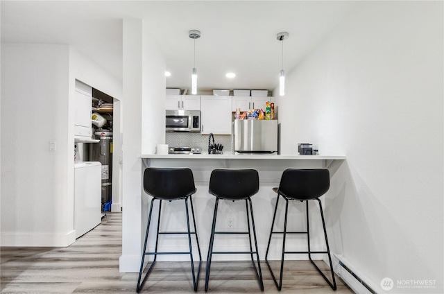 kitchen with a breakfast bar area, stainless steel appliances, backsplash, white cabinetry, and washer / dryer