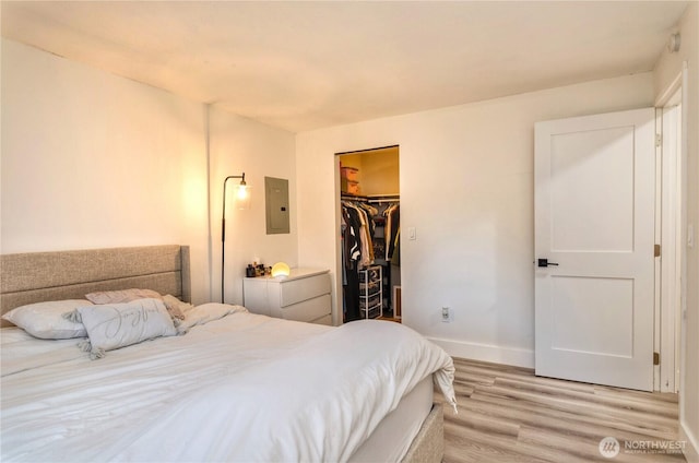 bedroom with light wood finished floors, electric panel, baseboards, a spacious closet, and a closet