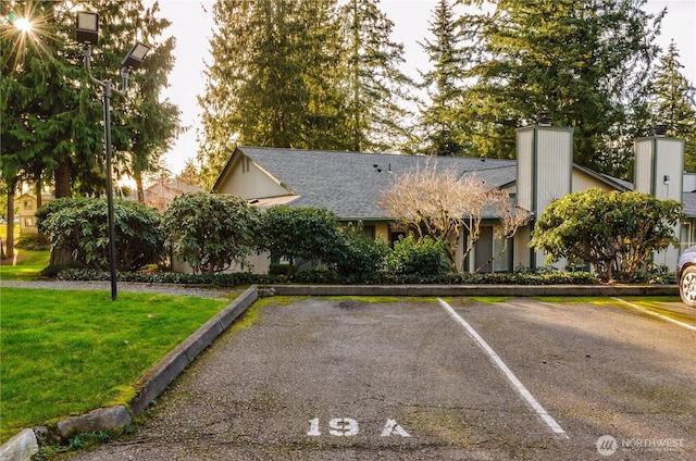 view of front of property featuring uncovered parking, a front lawn, and roof with shingles