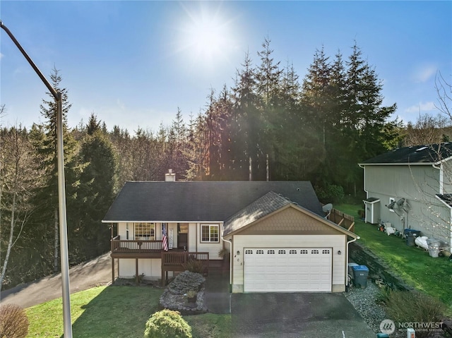 view of front of home with driveway, a garage, a wooded view, and a front yard