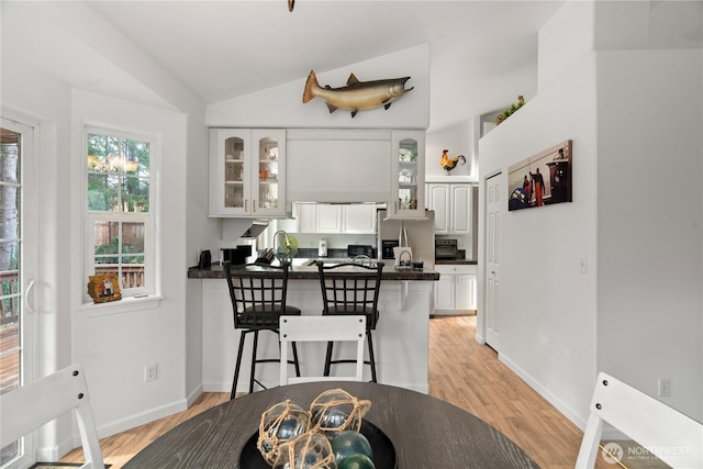 dining space featuring light wood-type flooring, lofted ceiling, and baseboards
