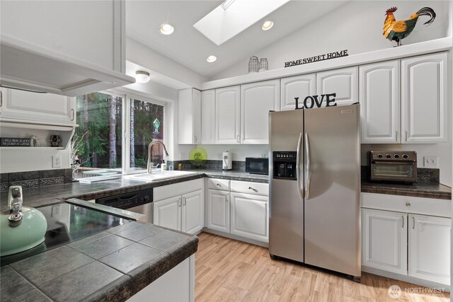 kitchen with stainless steel appliances, white cabinets, a sink, and lofted ceiling with skylight