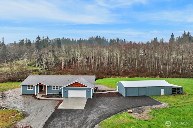 view of front of home with driveway, a forest view, a front lawn, and an outdoor structure